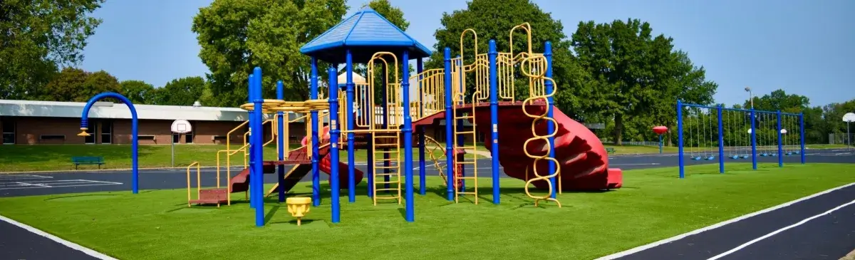 Artificial playground grass with blue and yellow playground equipment